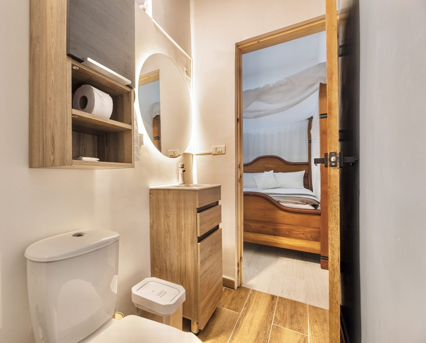 Baño de Casa Luz con espejo redondo retroiluminado y vista al dormitorio